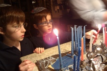 Two boys stand in front of Hanukkah candles.