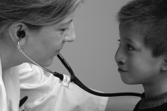 Medical professional holds stethoscope to patient's chest.