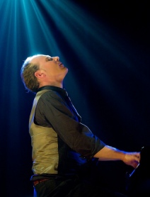Man has light shining down on him while he performs on stage.