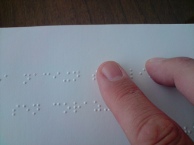 Two fingers read Braille on a page.