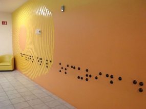 Large Braille makes a line across a full wall with some round tactile elements on the wall as well.