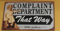 Sign shows little girl pointing away and says: Complaint Department that way 200 miles.