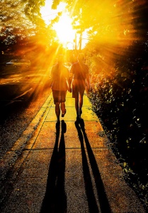 Sun shines brightly on a couple walking down the street holding hands.