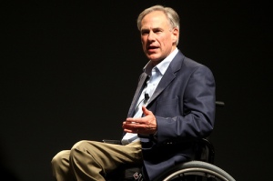 Governor Greg Abbott is speaking, the top rim of his wheelchair is visible.