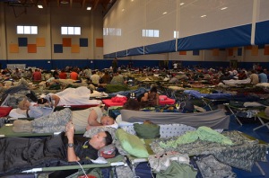 Gym with hundreds of people laying on the floor in sleeping bags.