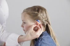 Adult puts a blue hearing aid on a young girl.