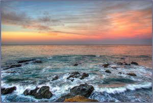 Picture of sunset with waves skimming over rocks in the water.